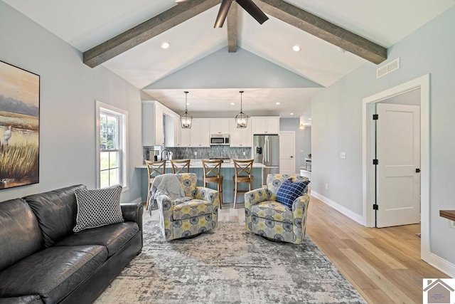 living room with high vaulted ceiling, ceiling fan, light hardwood / wood-style floors, and beam ceiling