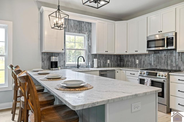 kitchen featuring light wood-type flooring, backsplash, stainless steel appliances, decorative light fixtures, and sink