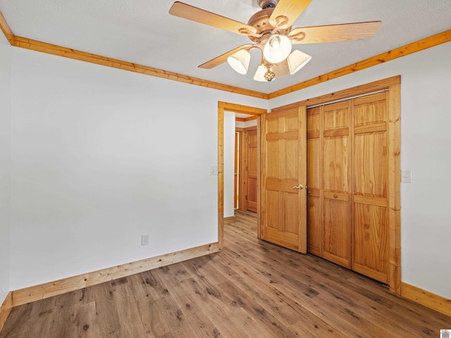 unfurnished bedroom featuring a textured ceiling, a closet, wood-type flooring, ornamental molding, and ceiling fan