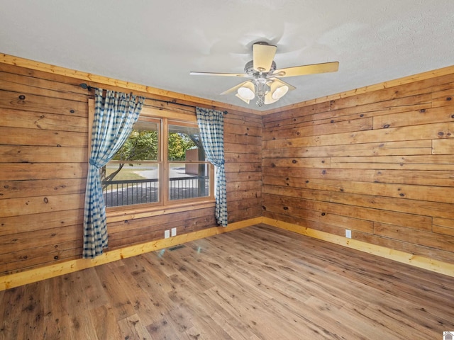 spare room with hardwood / wood-style floors, ceiling fan, wood walls, and a textured ceiling