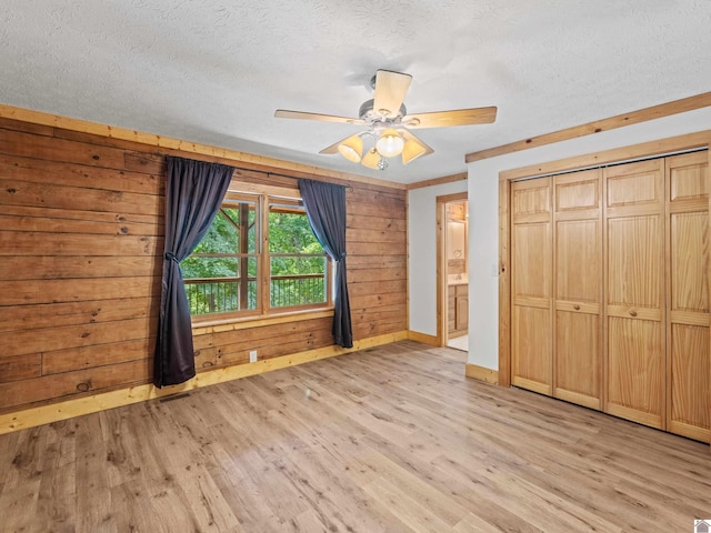 unfurnished bedroom with a textured ceiling, light hardwood / wood-style flooring, ceiling fan, and wood walls