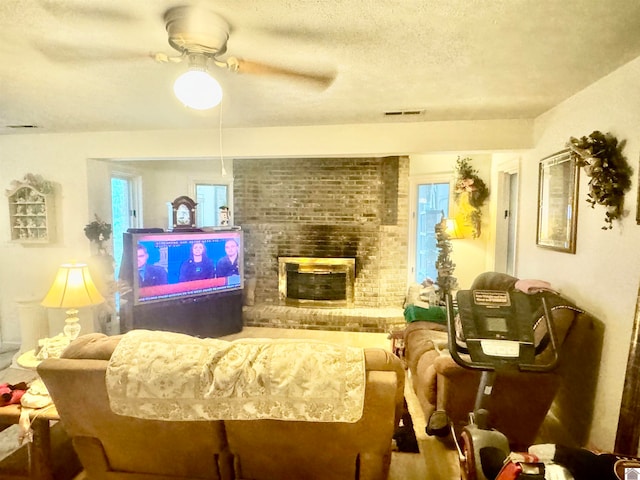 living room featuring a textured ceiling, ceiling fan, and a brick fireplace