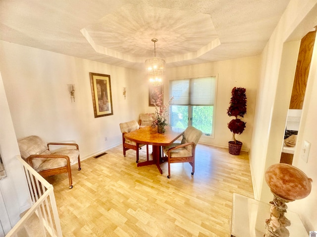 dining area featuring light hardwood / wood-style floors, a notable chandelier, and a tray ceiling