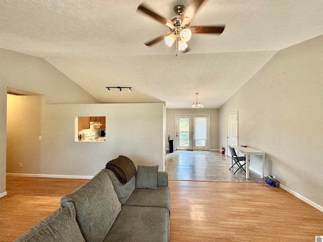 living room featuring a textured ceiling, light hardwood / wood-style flooring, vaulted ceiling, and ceiling fan with notable chandelier