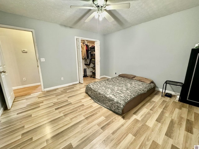 bedroom featuring light hardwood / wood-style floors, ceiling fan, a spacious closet, and a textured ceiling