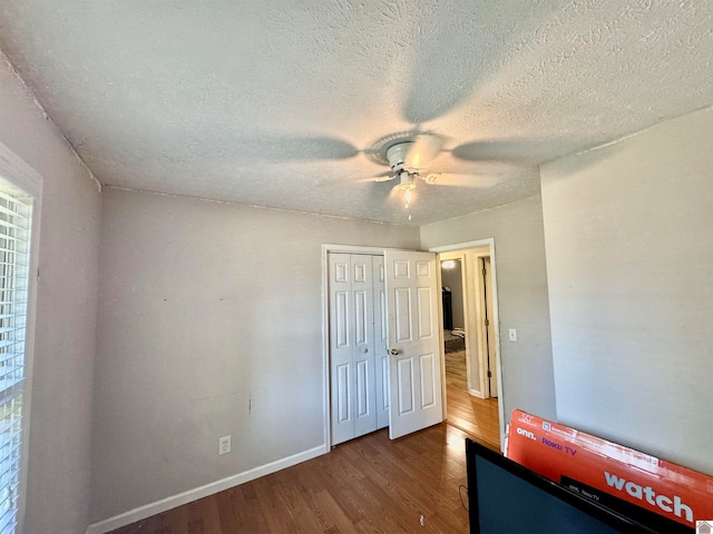 unfurnished bedroom with a textured ceiling, a closet, dark wood-type flooring, ceiling fan, and multiple windows