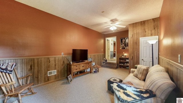 carpeted living room with a textured ceiling, ceiling fan, and wooden walls