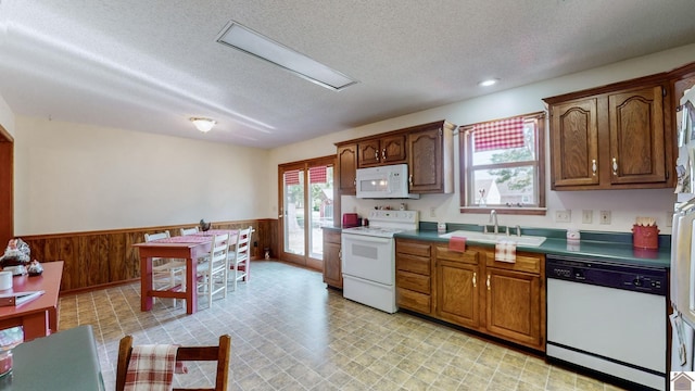 kitchen featuring a textured ceiling, white appliances, sink, a skylight, and wooden walls