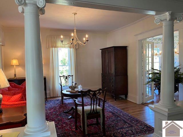 dining area featuring hardwood / wood-style flooring, ornamental molding, a chandelier, and decorative columns