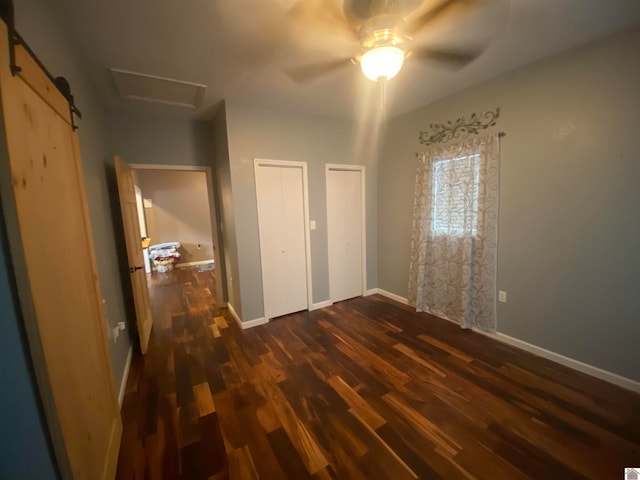 unfurnished bedroom with multiple closets, dark hardwood / wood-style flooring, ceiling fan, and a barn door