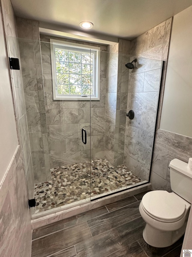 full bath with a stall shower, wainscoting, tile walls, and toilet