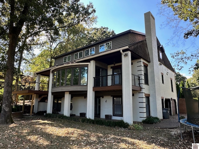 exterior space featuring a balcony, a trampoline, a chimney, and brick siding