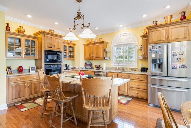 kitchen with light hardwood / wood-style flooring, black appliances, sink, a center island, and light stone countertops