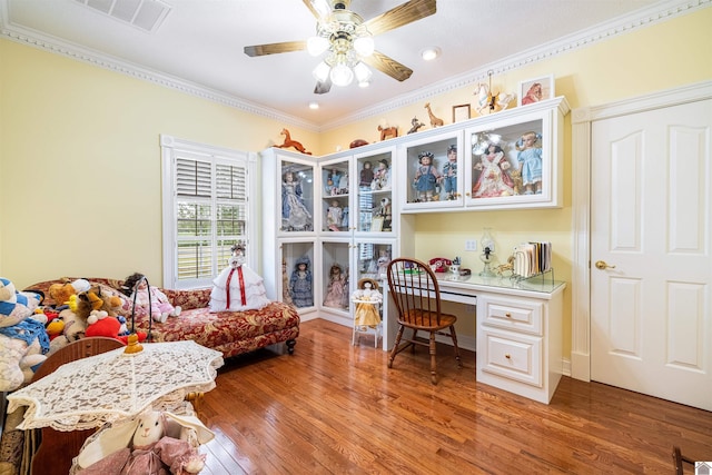 office with hardwood / wood-style floors, ceiling fan, built in desk, and crown molding