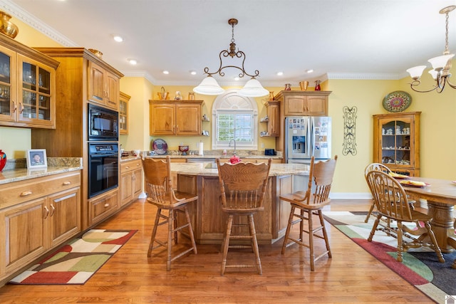 kitchen featuring a chandelier, light hardwood / wood-style flooring, black appliances, light stone counters, and a center island