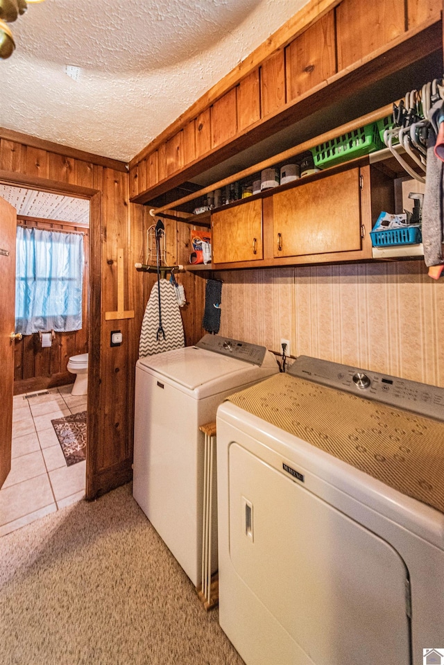 laundry area featuring washer and dryer, wood walls, light tile patterned floors, and a textured ceiling