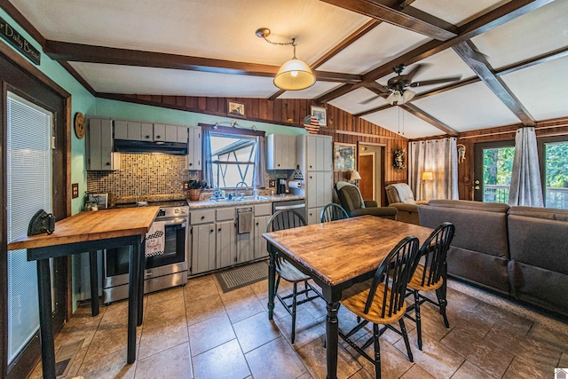 interior space featuring vaulted ceiling with beams, a wealth of natural light, ceiling fan, and stainless steel range oven