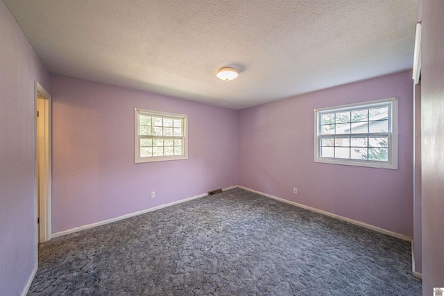 unfurnished room with a textured ceiling, a wealth of natural light, and dark colored carpet