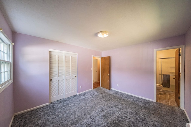 unfurnished bedroom with a closet, dark colored carpet, a textured ceiling, and ensuite bath