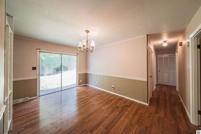 spare room with a textured ceiling, an inviting chandelier, and dark hardwood / wood-style flooring