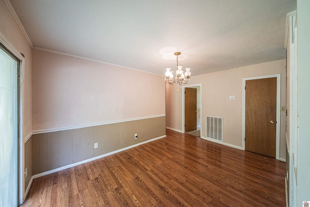 spare room with a textured ceiling, wood walls, dark hardwood / wood-style flooring, a notable chandelier, and ornamental molding