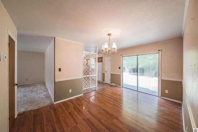 empty room featuring a textured ceiling, hardwood / wood-style floors, a chandelier, wood walls, and ornamental molding