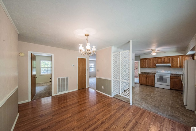 unfurnished living room with ceiling fan with notable chandelier, dark hardwood / wood-style flooring, a textured ceiling, and a healthy amount of sunlight