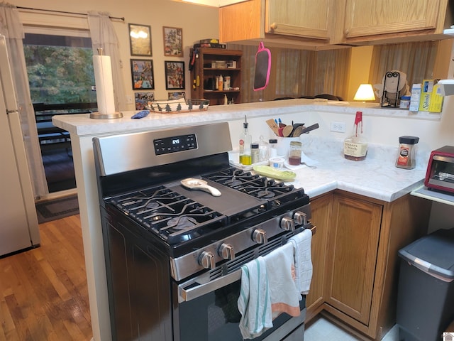 kitchen featuring hardwood / wood-style flooring, stainless steel gas range oven, kitchen peninsula, and white fridge