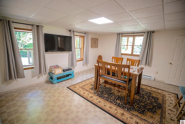 dining room with a baseboard heating unit, a healthy amount of sunlight, and a drop ceiling