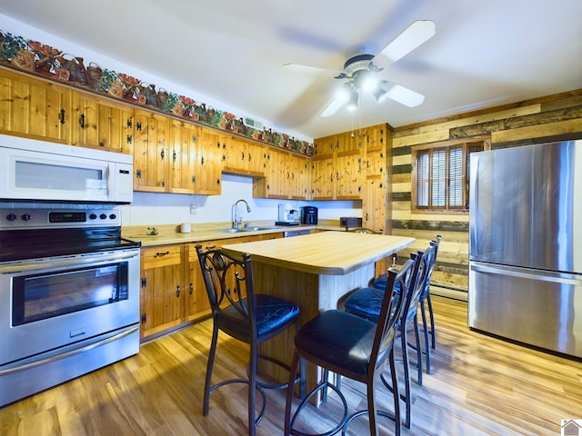 kitchen with light hardwood / wood-style floors, wooden walls, appliances with stainless steel finishes, baseboard heating, and ceiling fan