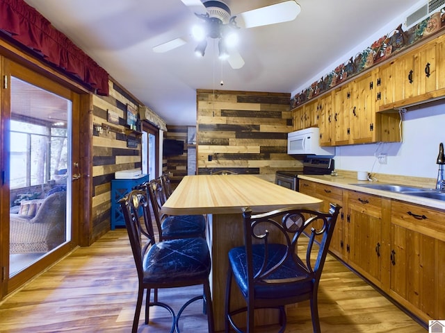 kitchen featuring sink, wood walls, light hardwood / wood-style flooring, stainless steel range with electric stovetop, and ceiling fan