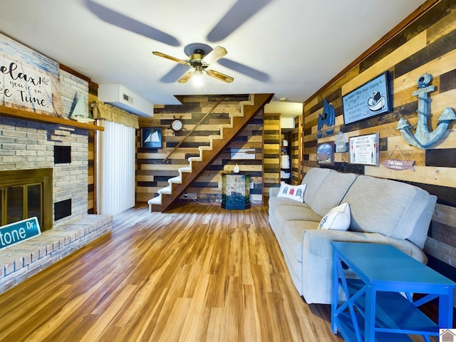 living room featuring a brick fireplace, light wood-type flooring, wood walls, and ceiling fan