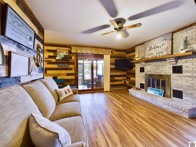 living room featuring a brick fireplace, ceiling fan, hardwood / wood-style floors, and wooden walls