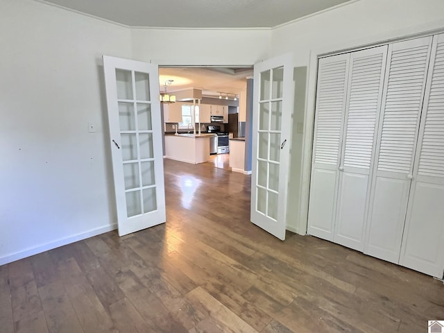 interior space with a sink, french doors, baseboards, ornamental molding, and dark wood-style floors
