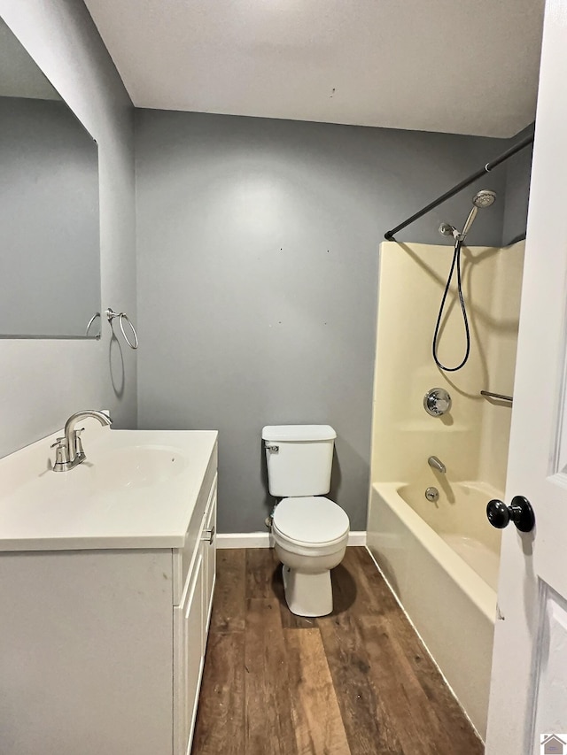 bathroom with wood finished floors, toilet, vanity, tub / shower combination, and baseboards