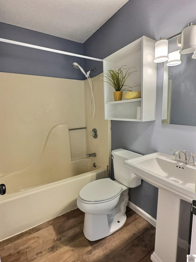 bathroom with wood finished floors, toilet, baseboards, and shower / washtub combination