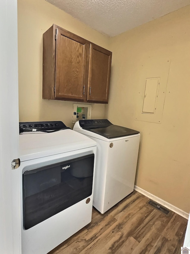 clothes washing area with electric panel, a textured ceiling, cabinets, hardwood / wood-style flooring, and washer and dryer