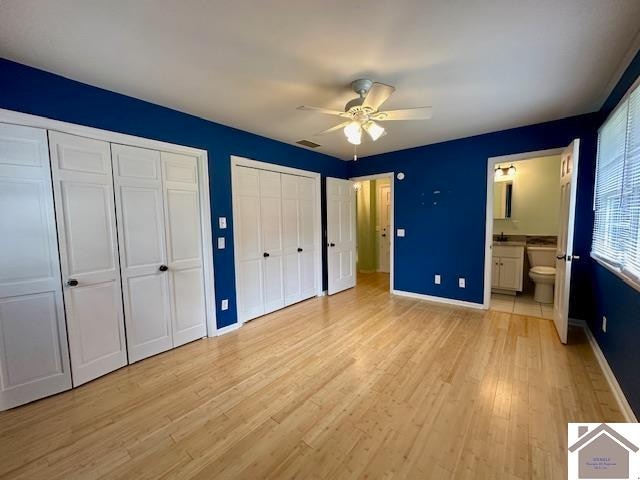 unfurnished bedroom with light hardwood / wood-style floors, ceiling fan, ensuite bathroom, and multiple closets