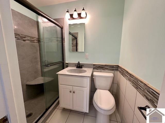 bathroom with vanity, a shower with shower door, tile patterned floors, tile walls, and toilet