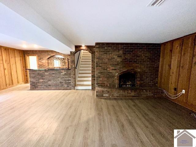 unfurnished living room featuring wood-type flooring, a fireplace, wood walls, and brick wall