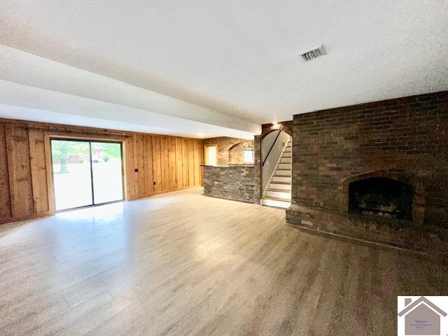 unfurnished living room featuring a brick fireplace, hardwood / wood-style flooring, and wooden walls