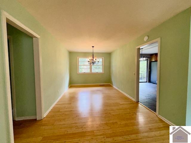 unfurnished room featuring light wood-type flooring and an inviting chandelier