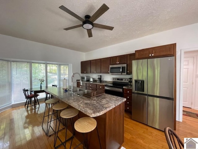 kitchen with light wood-type flooring, sink, an island with sink, a kitchen bar, and stainless steel appliances