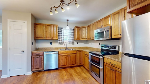 kitchen with pendant lighting, sink, light wood-type flooring, appliances with stainless steel finishes, and light stone counters