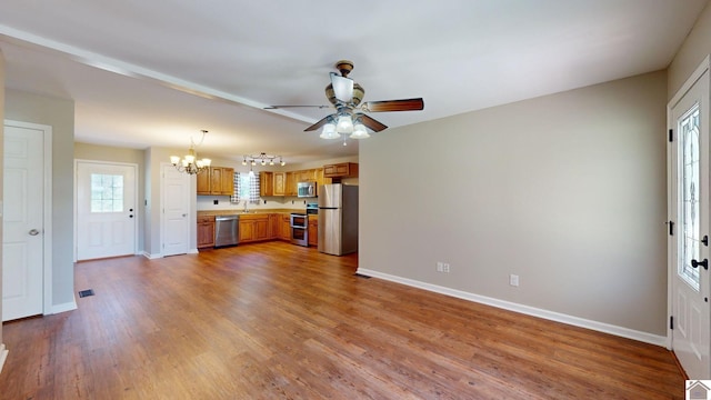 kitchen featuring sink, stainless steel appliances, pendant lighting, wood-type flooring, and ceiling fan with notable chandelier