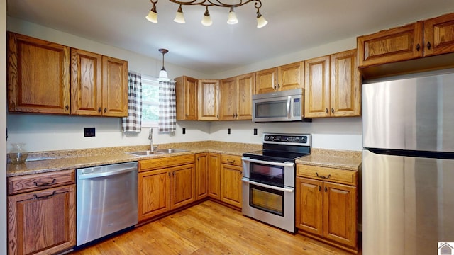 kitchen featuring sink, hanging light fixtures, stainless steel appliances, light stone counters, and light hardwood / wood-style flooring