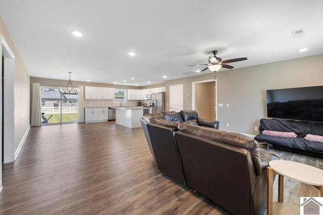 living room featuring ceiling fan with notable chandelier, dark wood-type flooring, and sink