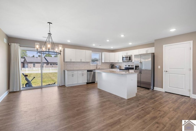 kitchen with appliances with stainless steel finishes, white cabinetry, a kitchen island, dark hardwood / wood-style flooring, and decorative light fixtures