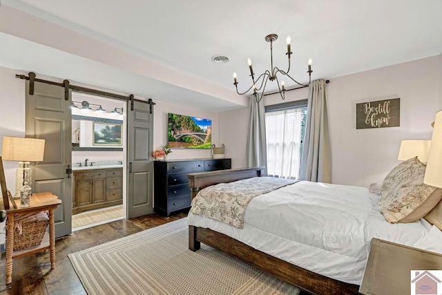 bedroom featuring an inviting chandelier, ensuite bathroom, dark wood-type flooring, and a barn door