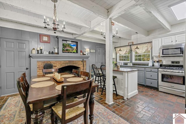 dining area with a fireplace, an inviting chandelier, beamed ceiling, and a skylight